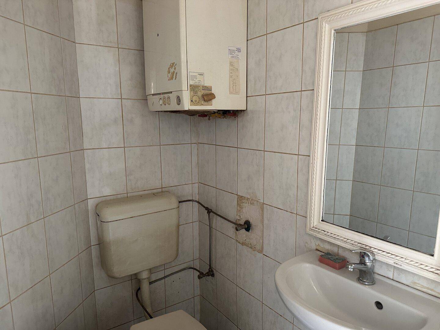 Kleines WC mit Waschbecken, Spiegel und Wandfliesen, inklusive Warmwasserboiler.