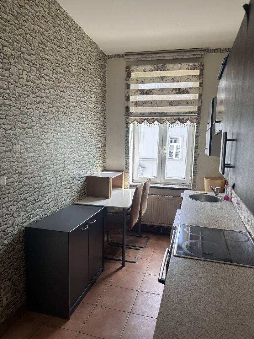 Kleine Küche mit dunklen Schränken, Mosaikfliesen und Essbereich am Fenster.