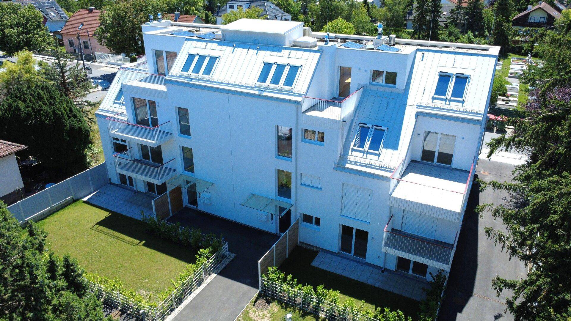 Luftaufnahme des weißen Wohnkomplexes mit Dachfenstern, Balkonen und umliegenden Gärten.