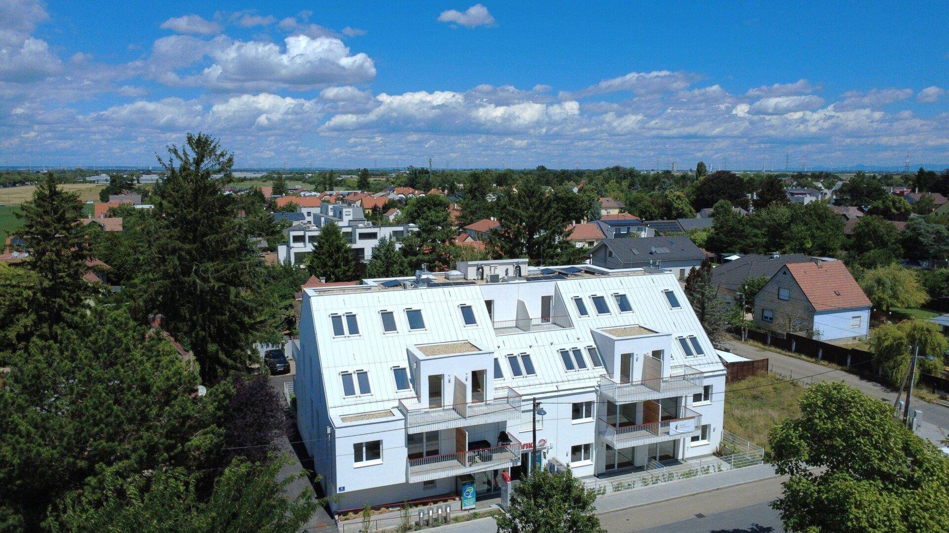 Panoramablick aus der Luft auf die moderne Wohnanlage, umgeben von Grünflächen und Einfamilienhäusern.