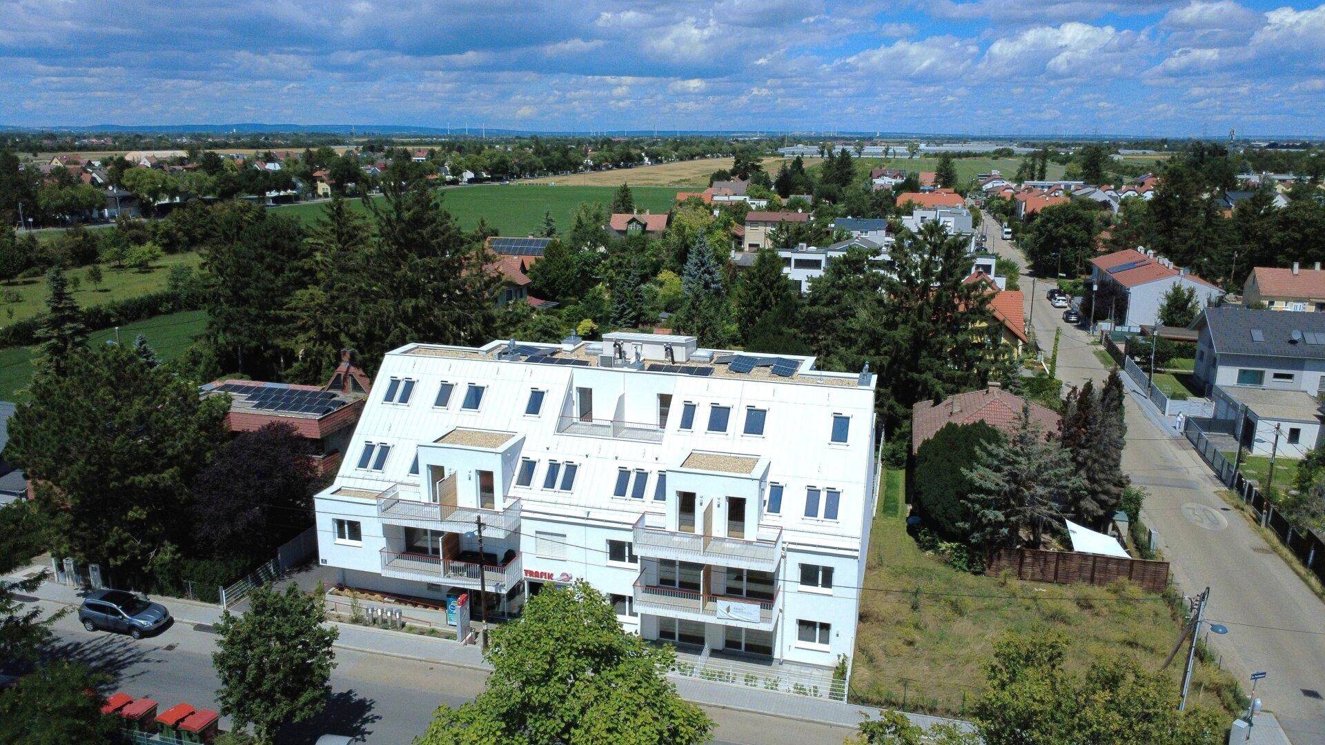 Die Wohnanlage aus der Vogelperspektive, eingebettet in eine grüne Landschaft mit weitem Horizont.
