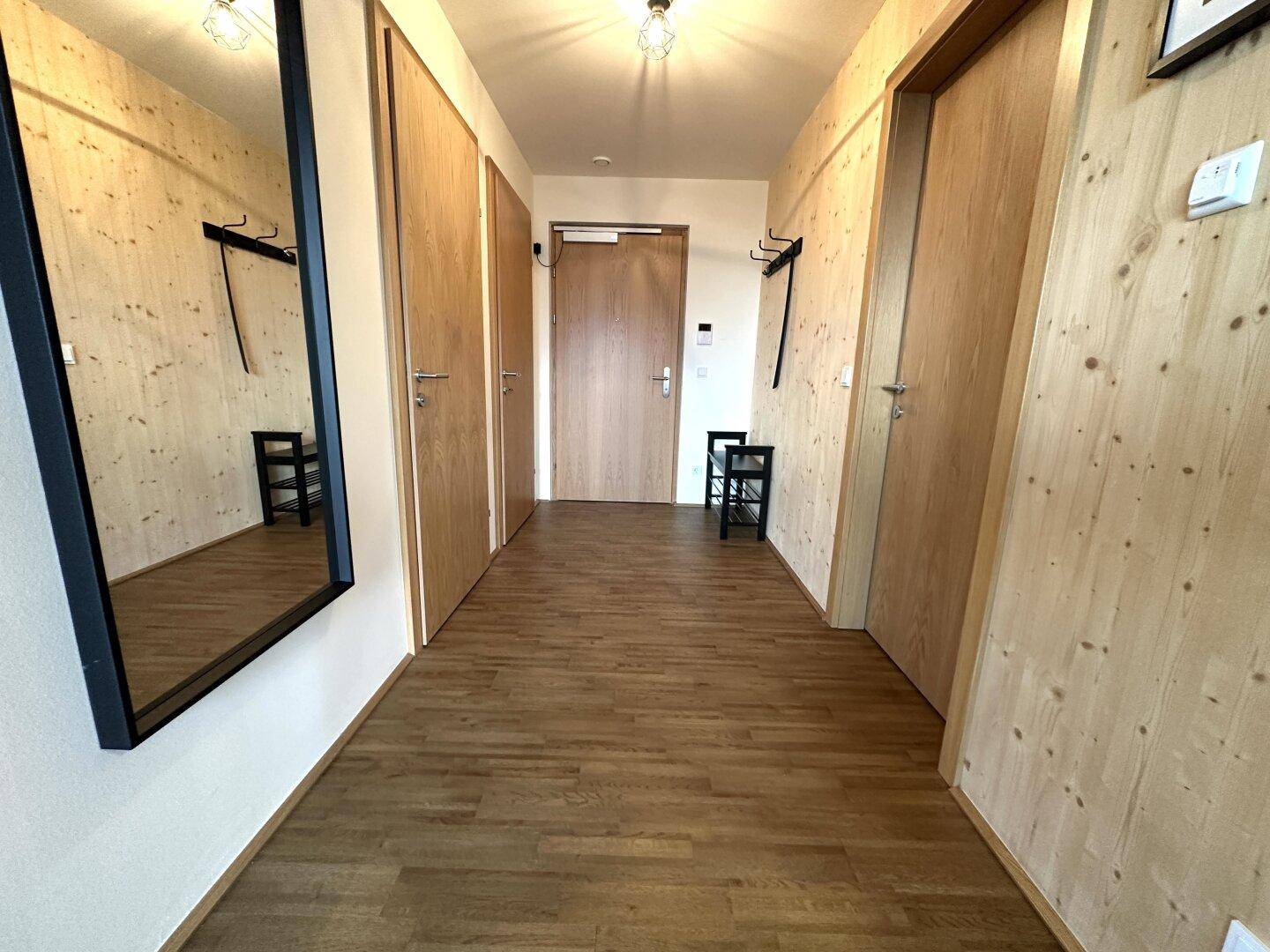 Heller Flur mit Holzboden, Holzverkleidung und einem großen Spiegel an der Wand.