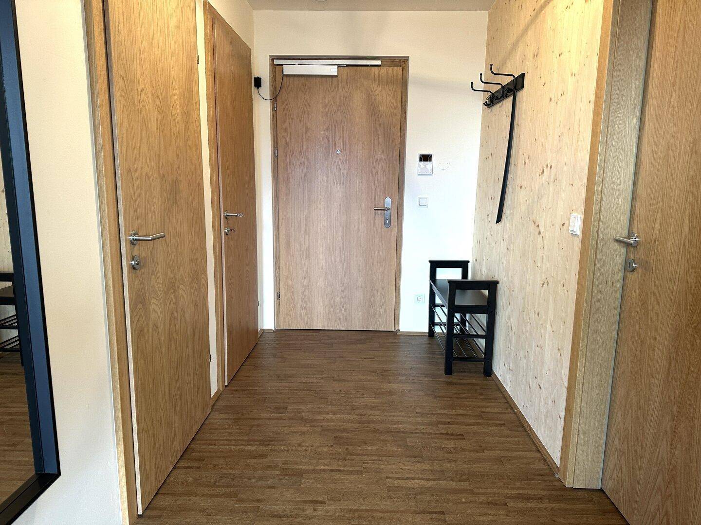 Eingangsbereich mit Holzboden, Garderobe und einer Sitzbank für Schuhe.