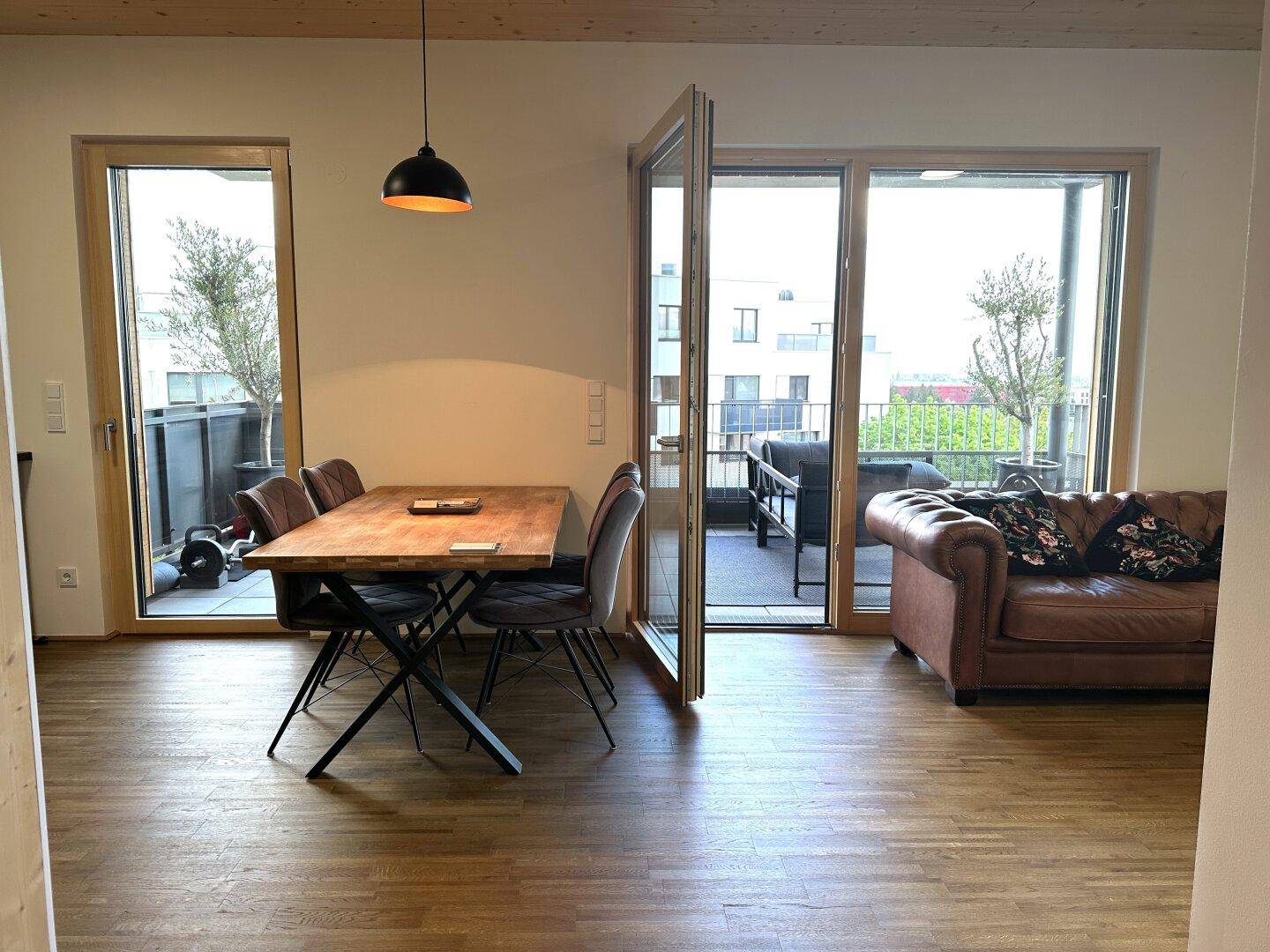 Geräumiger Wohn- und Essbereich mit Holzboden, Ledersofa und großen Fenstern zur Terrasse.