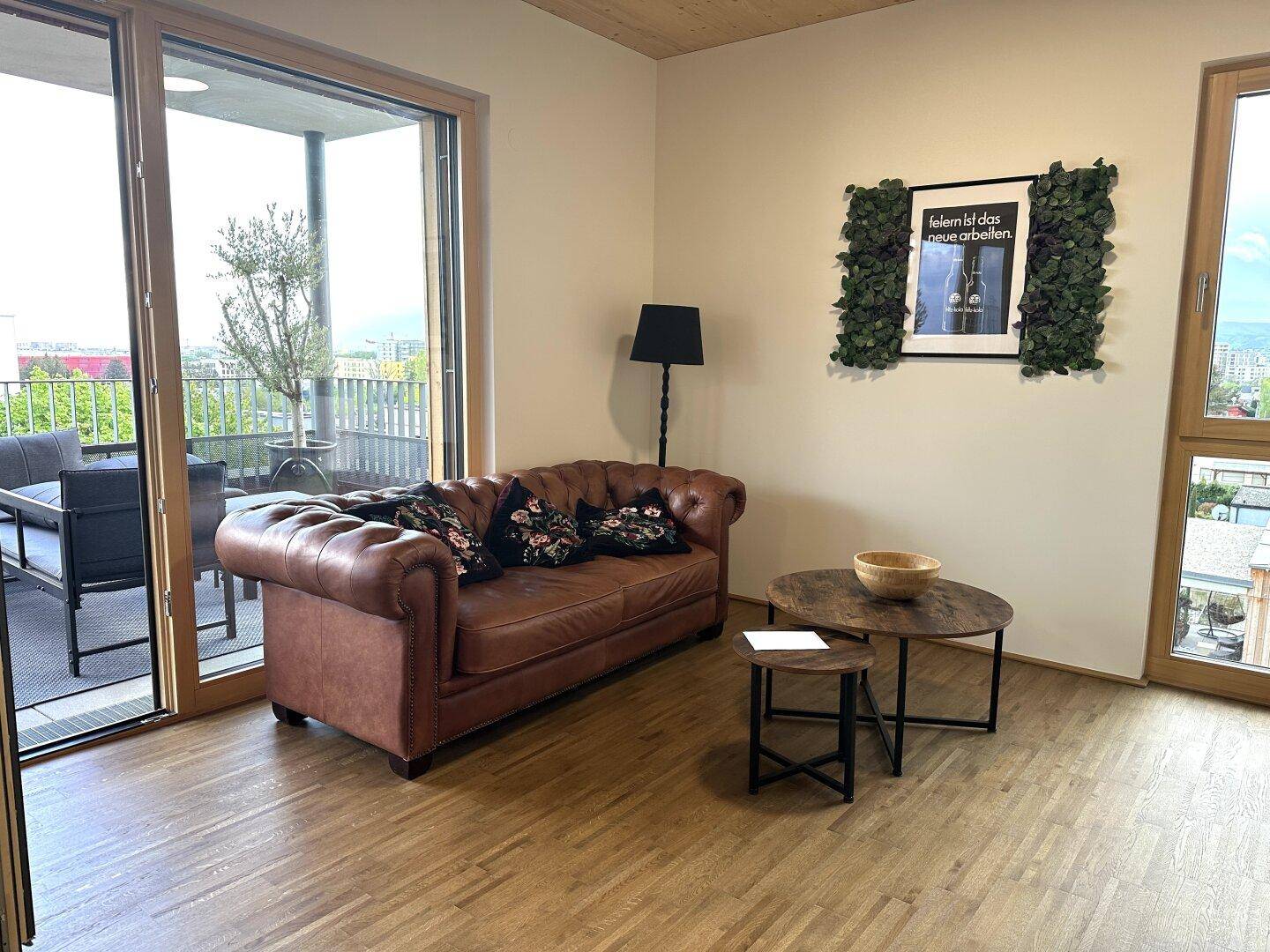 Gemütliches Wohnzimmer mit braunem Ledersofa, Holzboden und Zugang zu einer Außenterrasse.