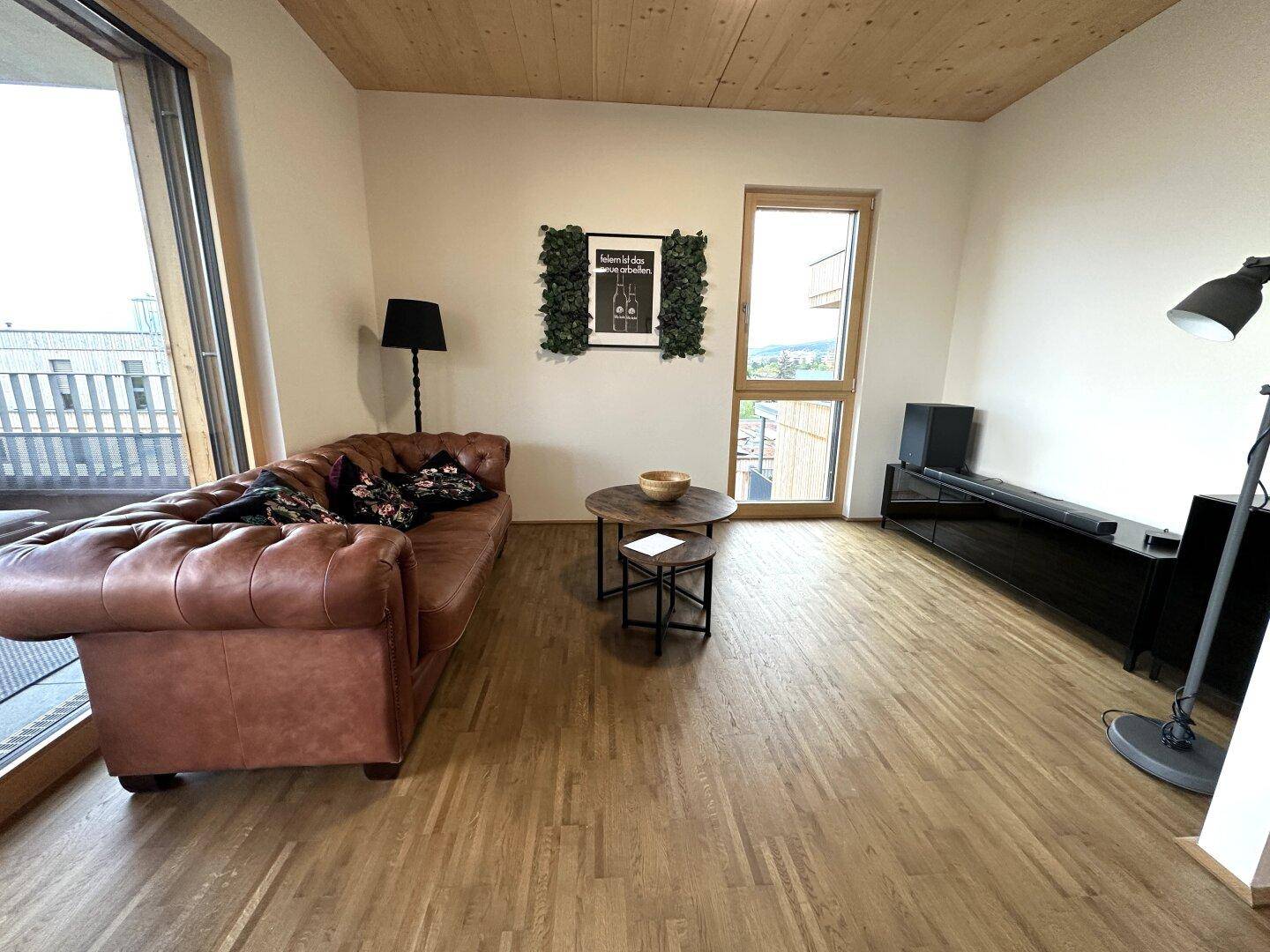 Modern eingerichtetes Wohnzimmer mit Holzboden, Ledersofa und großem Fenster mit Ausblick.