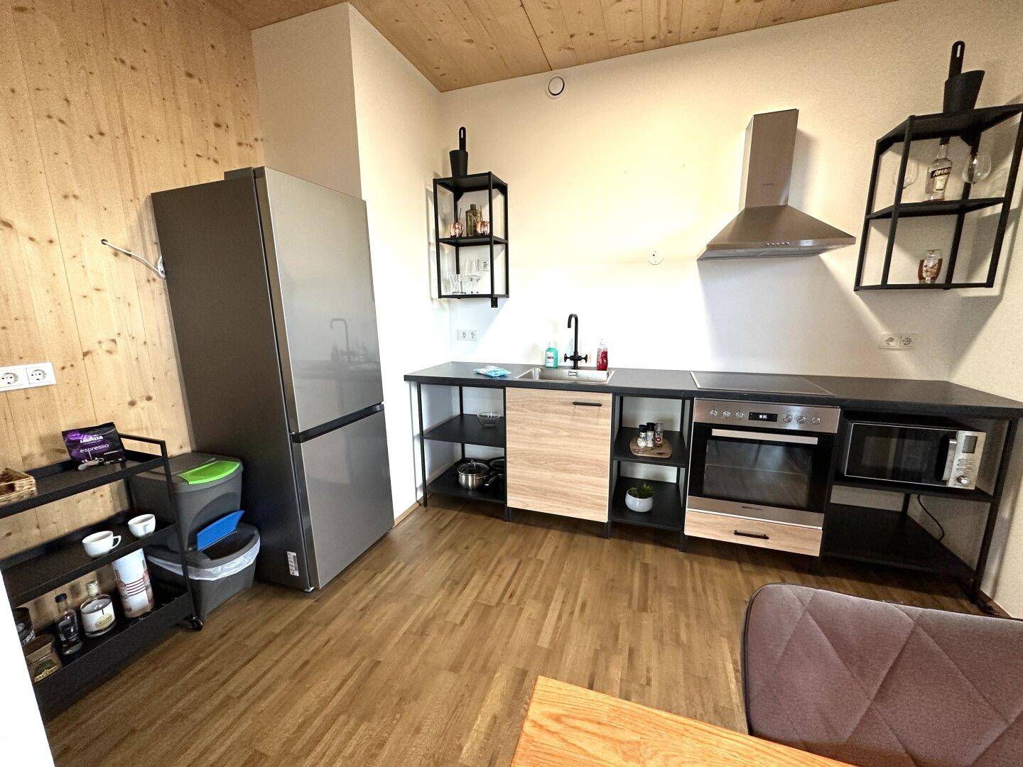 Funktionale Küche mit Holzboden, Edelstahlgeräten und offenen Regalen für zusätzlichen Stauraum.