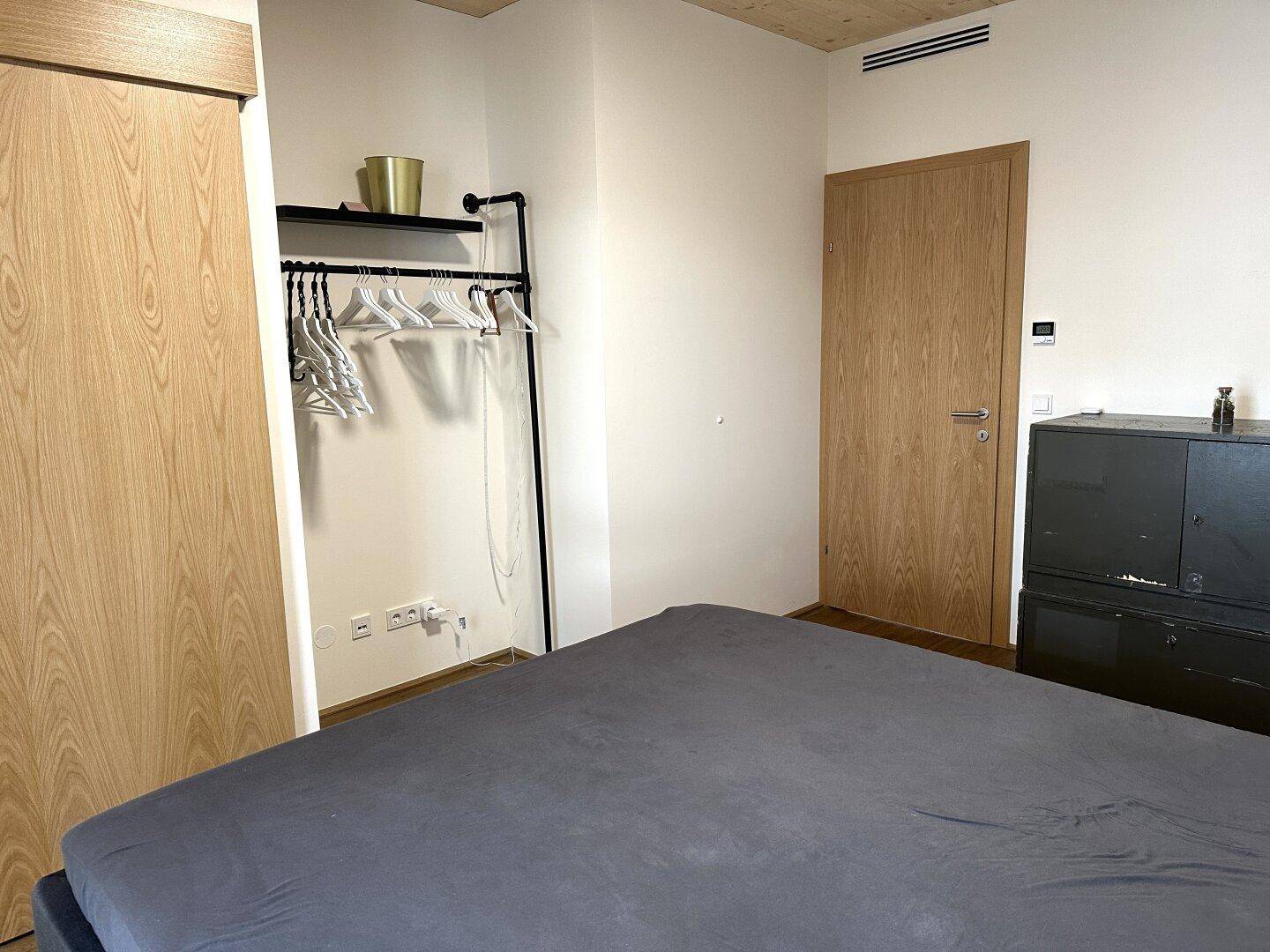 Schlafzimmer mit Holzboden, Kleiderstange und Schiebetür zum angrenzenden Badezimmer.