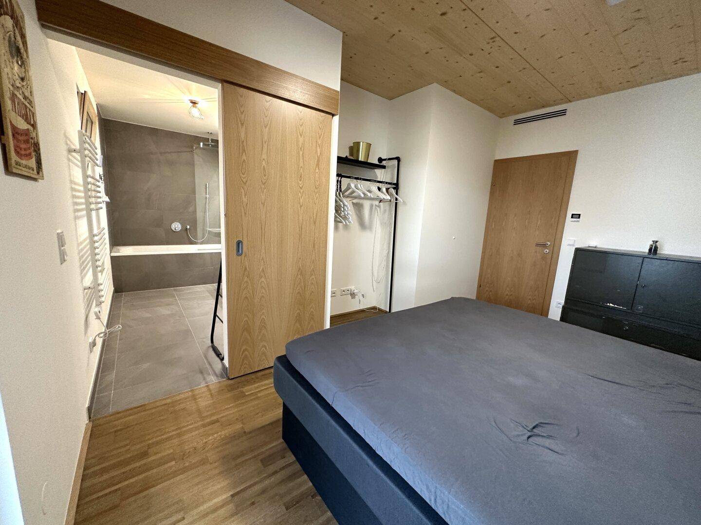 Schlafzimmer mit Holzboden und direktem Zugang zu einem modernen Badezimmer mit Badewanne.
