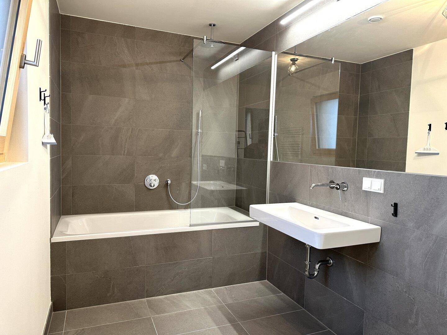 Modernes Badezimmer mit grauen Fliesen, Badewanne und separater Duschkabine.