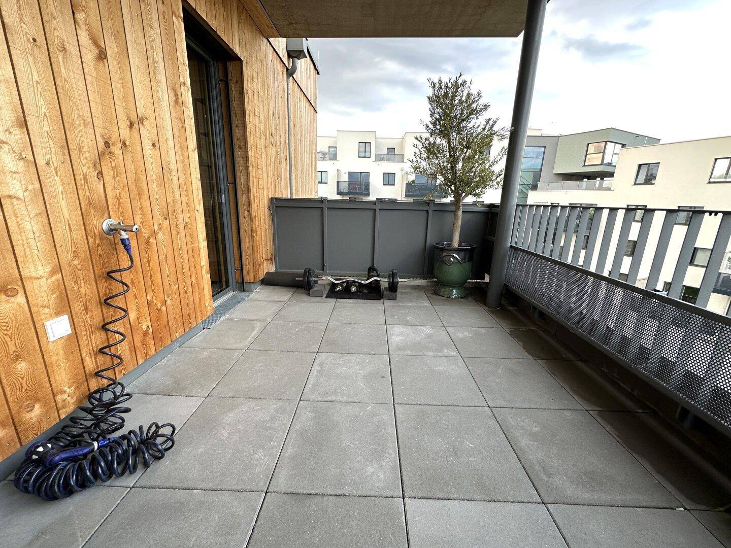 Funktionale Terrasse mit Fliesenboden, Trainingsgeräten und Anschluss für einen Wasserschlauch.