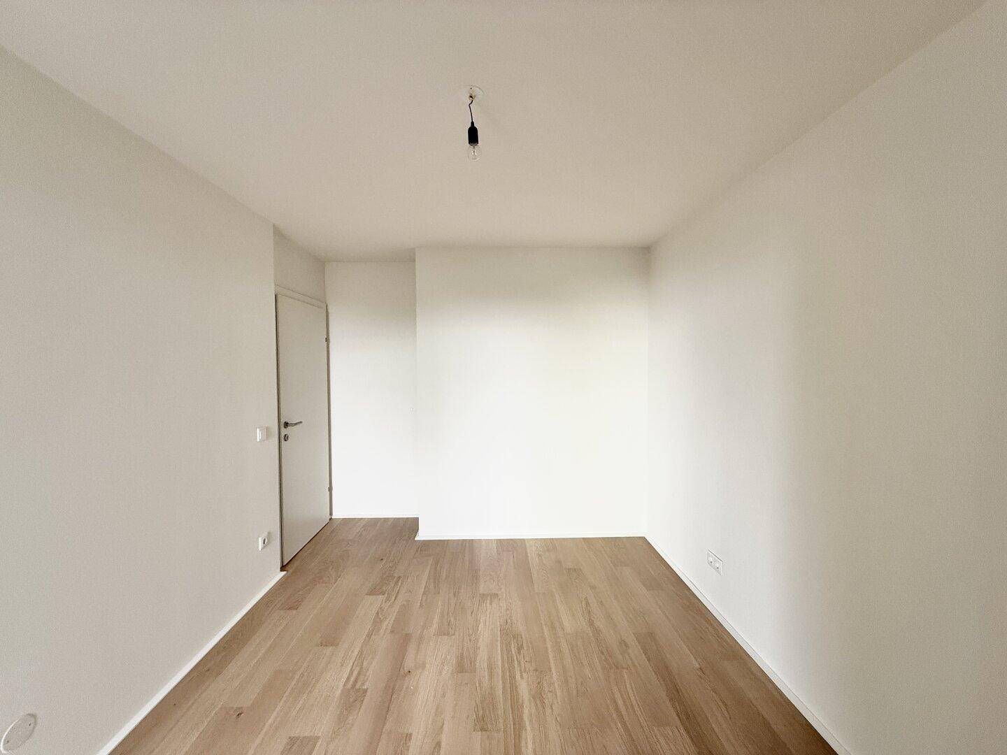 Unmöbliertes Schlafzimmer mit hellem Parkettboden und einer weißen Tür.