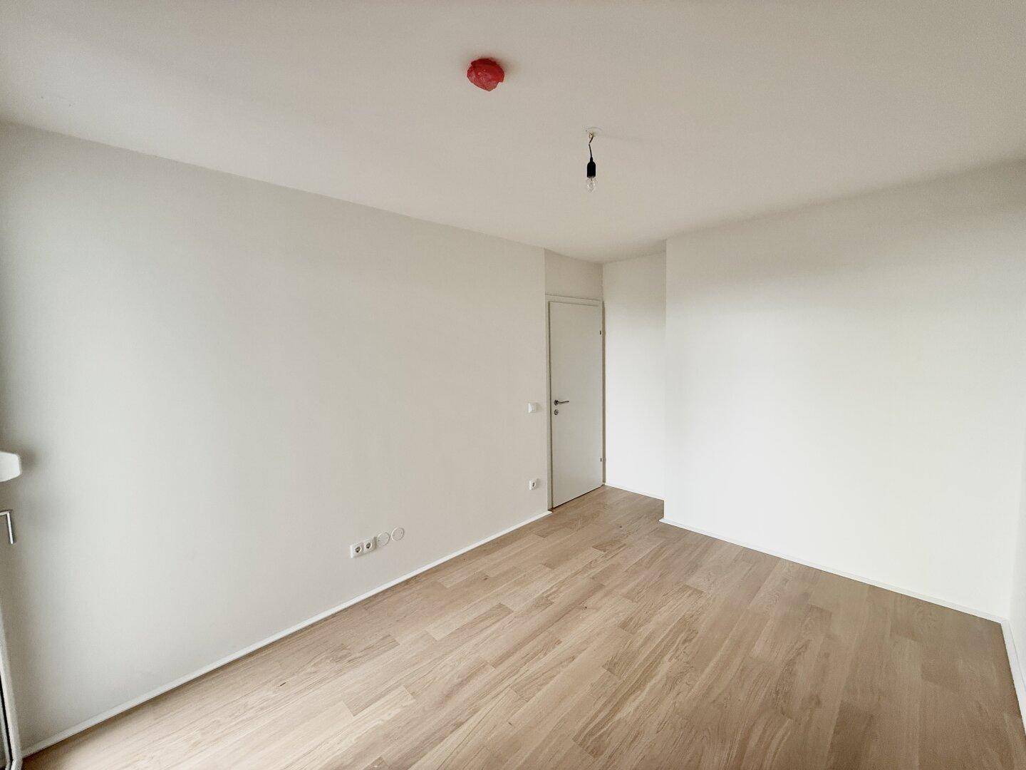 Geräumiges, unmöbliertes Zimmer mit Parkettboden und weiß gestrichenen Wänden.