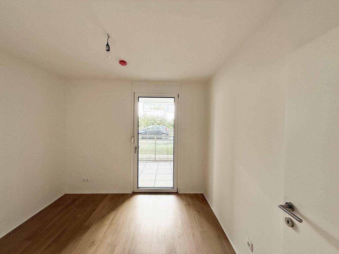 Helles Zimmer mit Parkettboden und Zugang zu einem Außenbereich, ideal als Schlafzimmer.