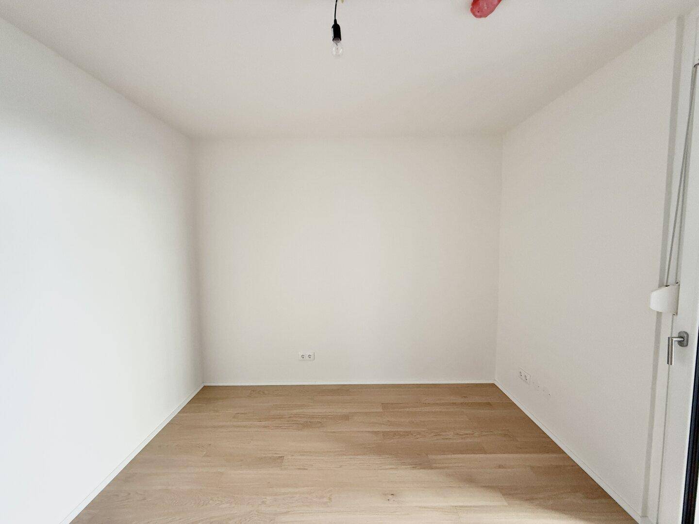 Leeres Zimmer mit hellem Parkettboden und weißen Wänden, bereit zur individuellen Gestaltung.