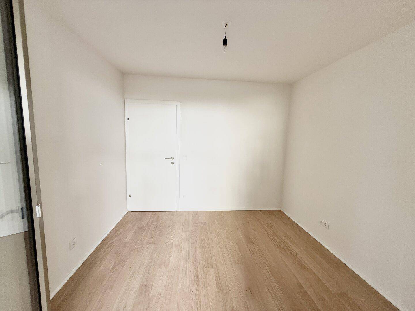 Unmöbliertes Zimmer mit Parkettboden und einer weißen Tür, ideal als Kinder- oder Gästezimmer.