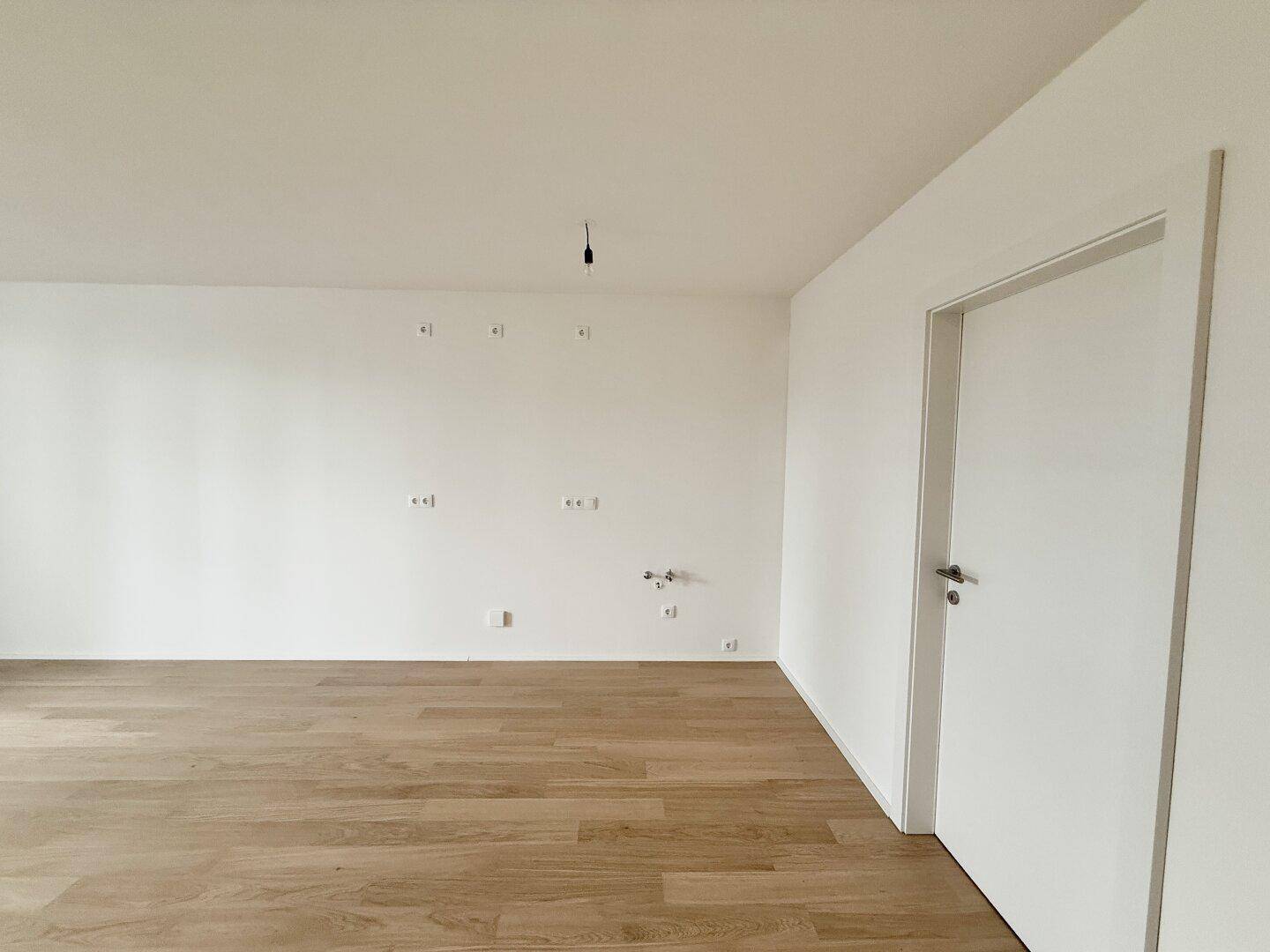 Geräumiges, unmöbliertes Wohnzimmer mit hellem Parkettboden und weißen Wänden.