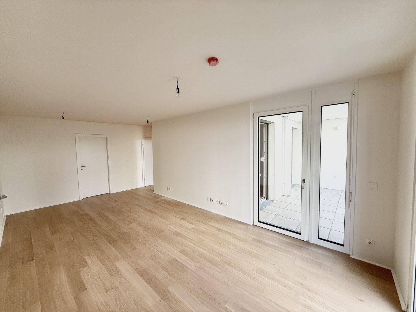 Lichtdurchfluteter Wohnbereich mit Parkettboden und großen Fenstertüren zum Außenbereich.
