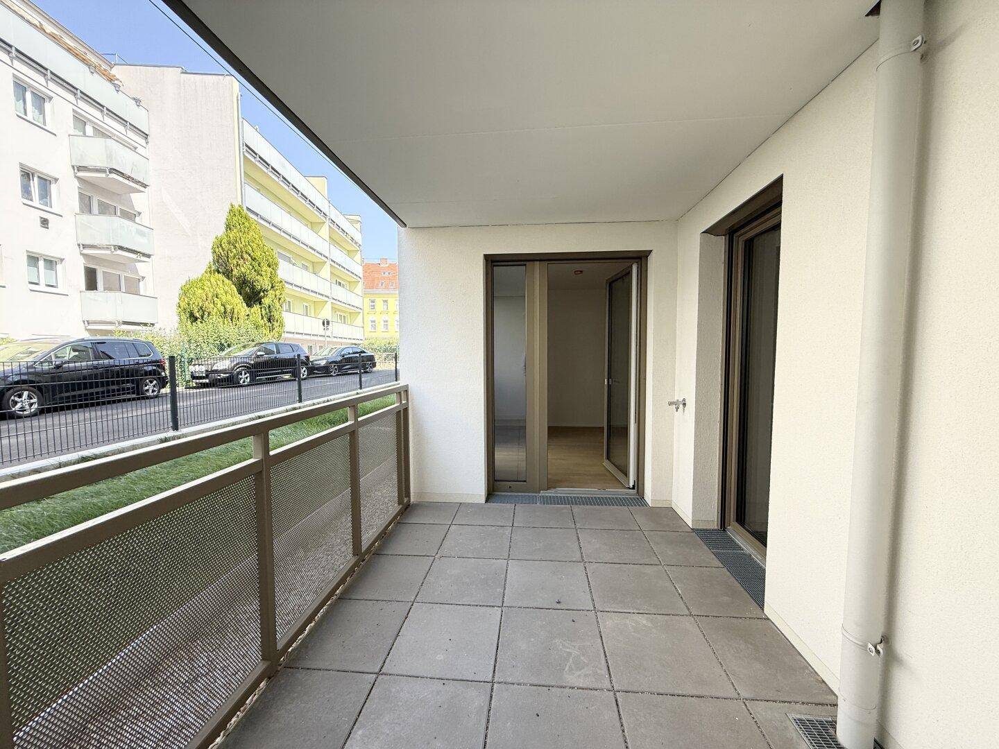 Heller Balkon mit Fliesenboden und Zugang zu den Innenräumen, umgeben von Grün.