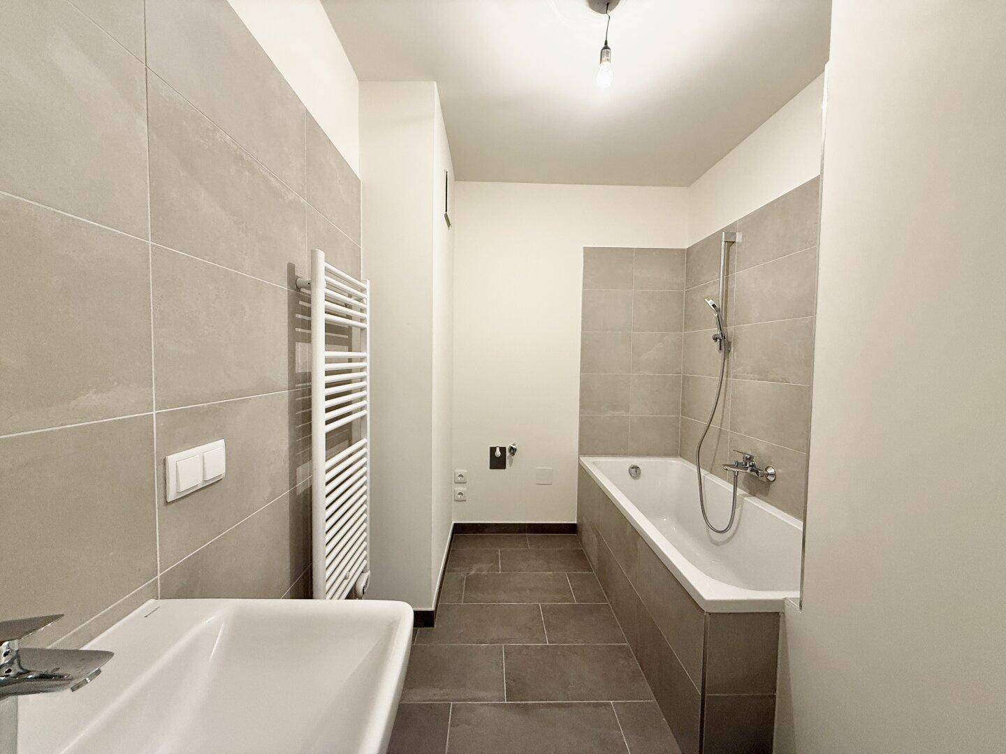 Modernes Badezimmer mit Badewanne, Waschbecken und beheiztem Handtuchhalter.