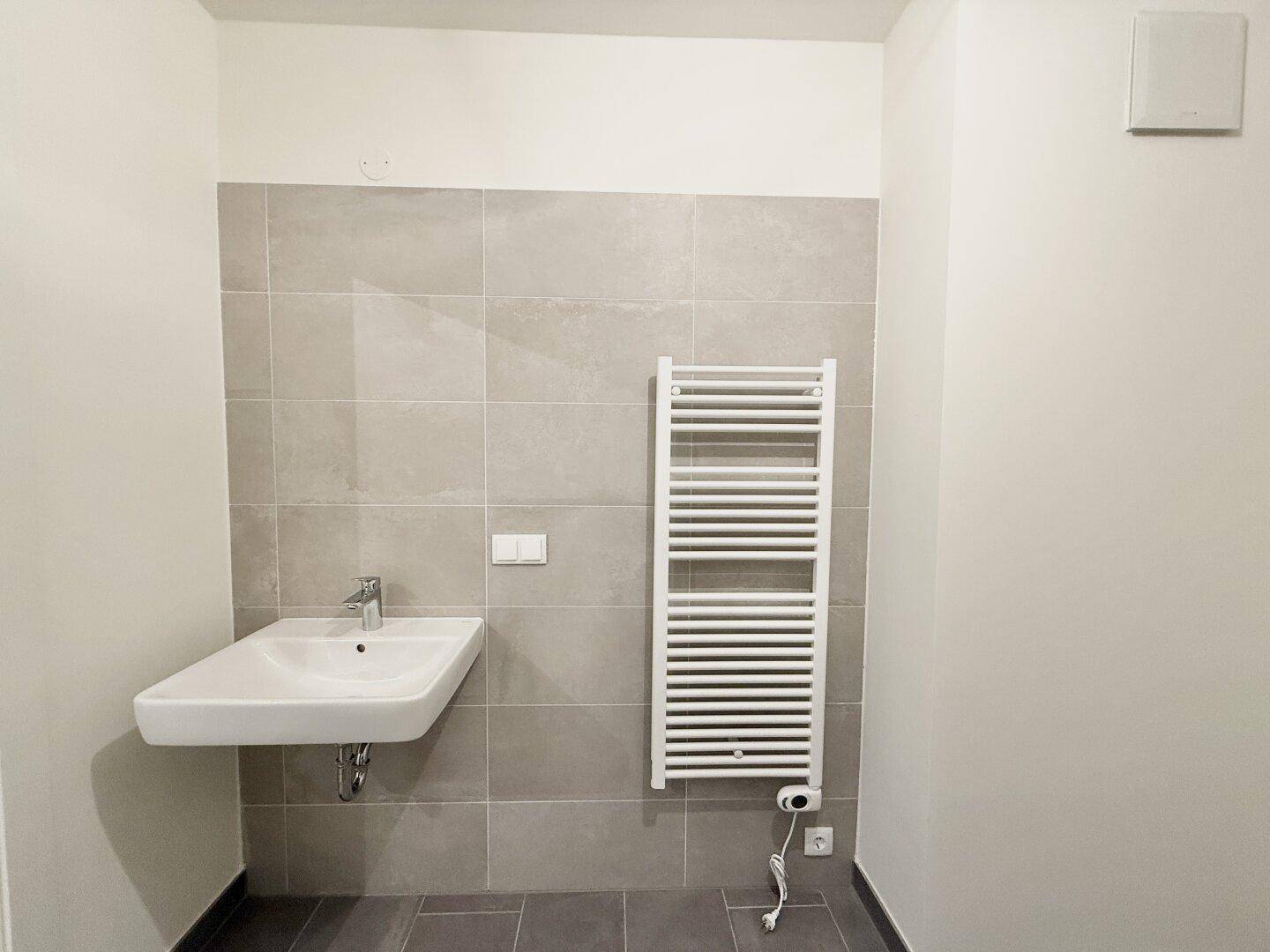 Modernes Badezimmer mit Waschbecken, beheiztem Handtuchhalter und hellen Fliesen.