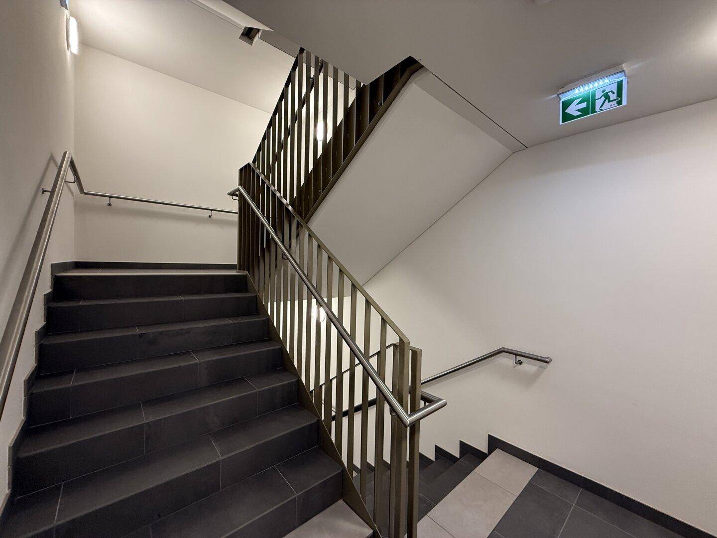 Modernes Treppenhaus mit dunklen Fliesen und Edelstahlgeländer in einem Mehrfamilienhaus.
