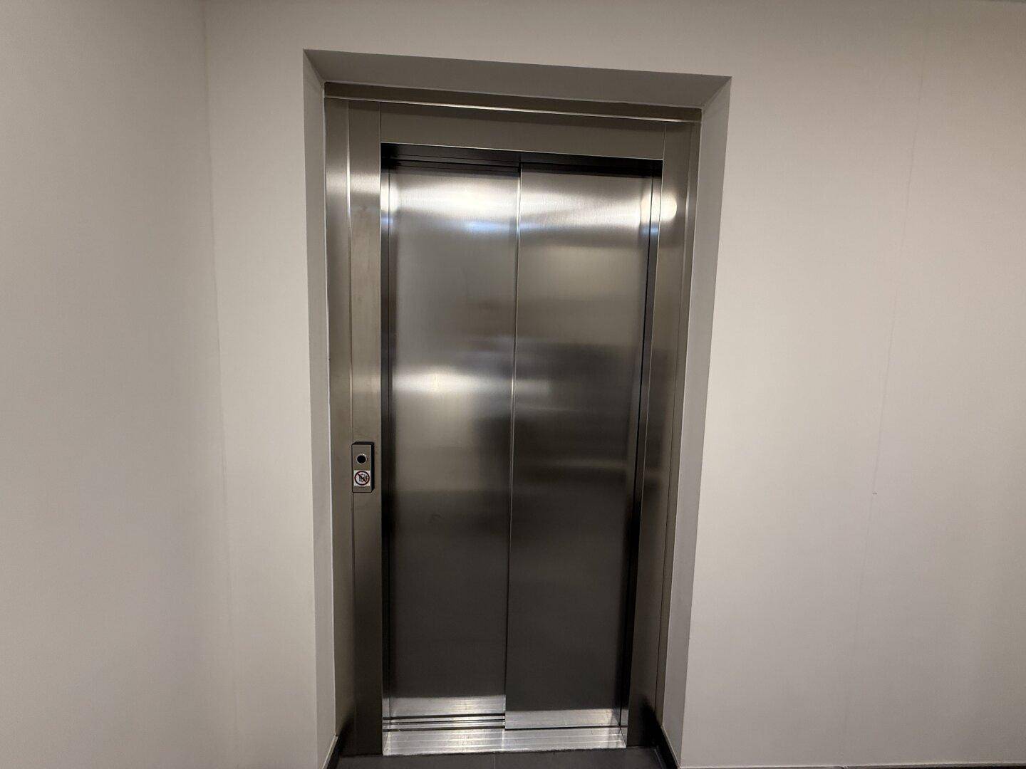 Moderner Aufzug mit Edelstahltüren in einem hellen Flur, bereit zur Nutzung.