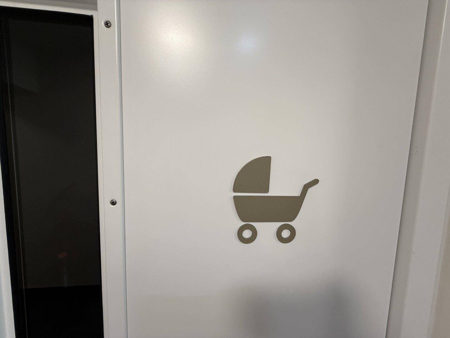 Weiße Tür mit Kinderwagensymbol, das auf einen speziellen Bereich für Familien hinweist.