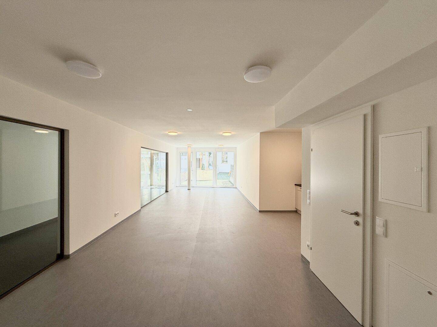 Geräumiger, heller Wohnbereich mit großen Fenstern und Zugang zu einem Außenbereich.