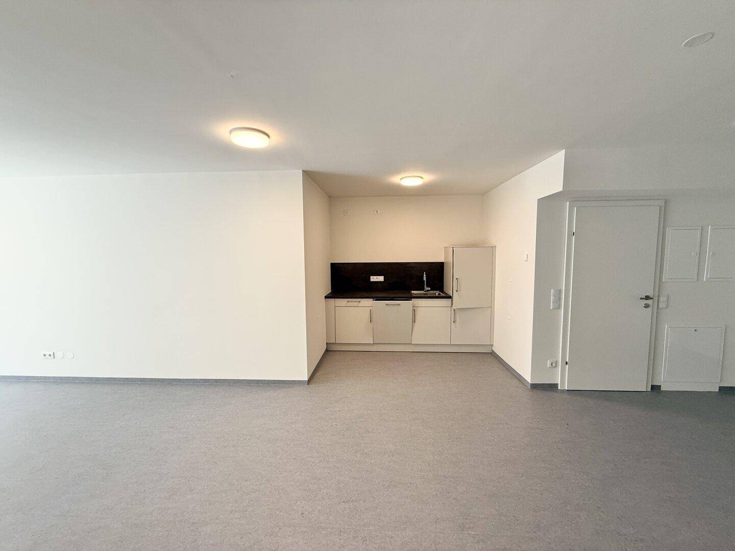 Einfache Küchenzeile mit weißen Schränken und dunkler Arbeitsplatte in einem leeren Raum.