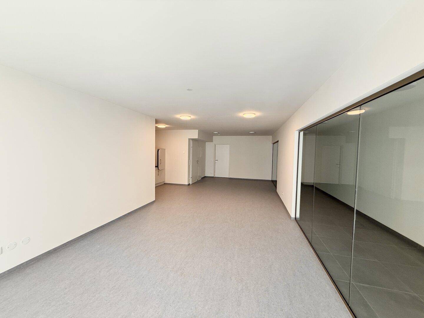 Weitläufiger, heller Wohnbereich mit moderner Glaswand und viel Tageslicht.