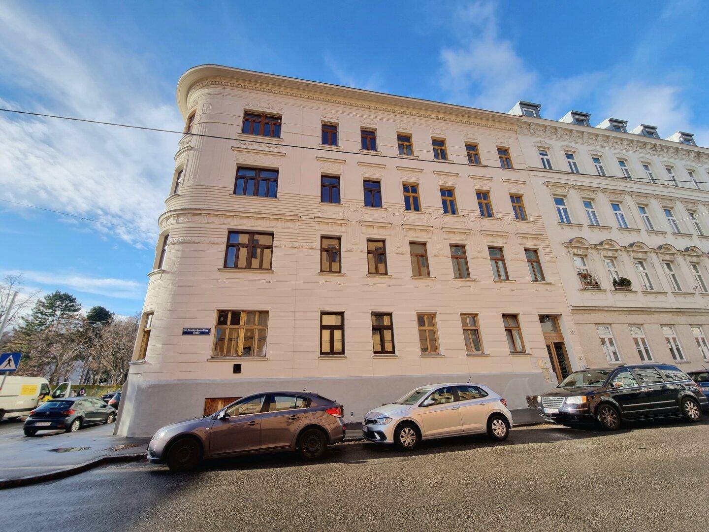 Klassisches Eckgebäude mit gepflegter Stuckfassade und vielen Fenstern in einer städtischen Umgebung.