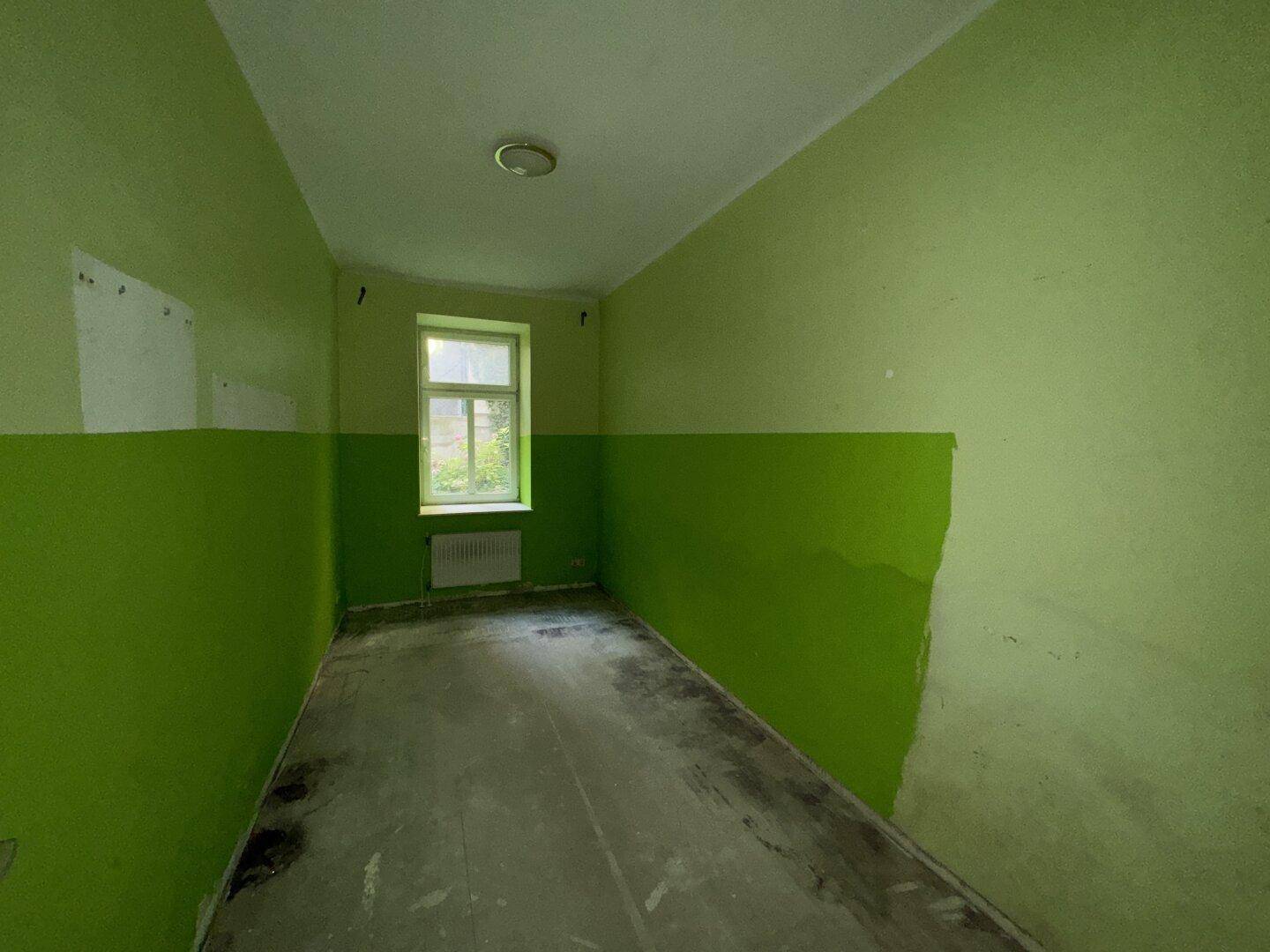 Unmöblierter Raum mit leuchtend grünen Wänden und Fenster, wartet auf die weitere Gestaltung.