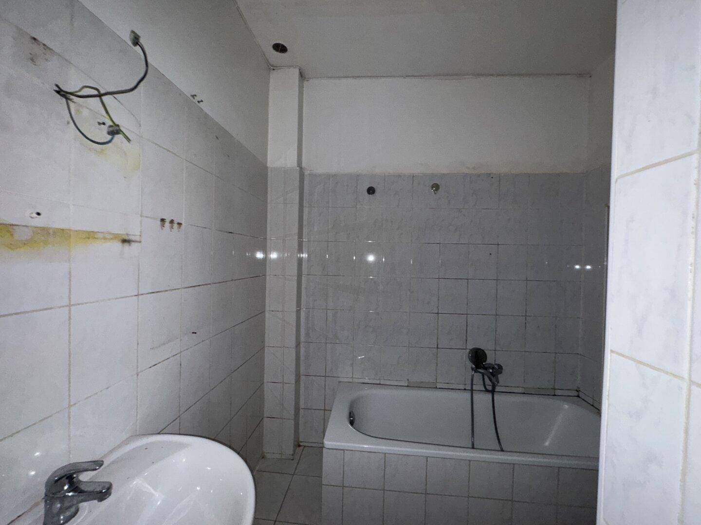 Badezimmer mit Badewanne und Waschbecken, gefliest und in renovierungsbedürftigem Zustand.