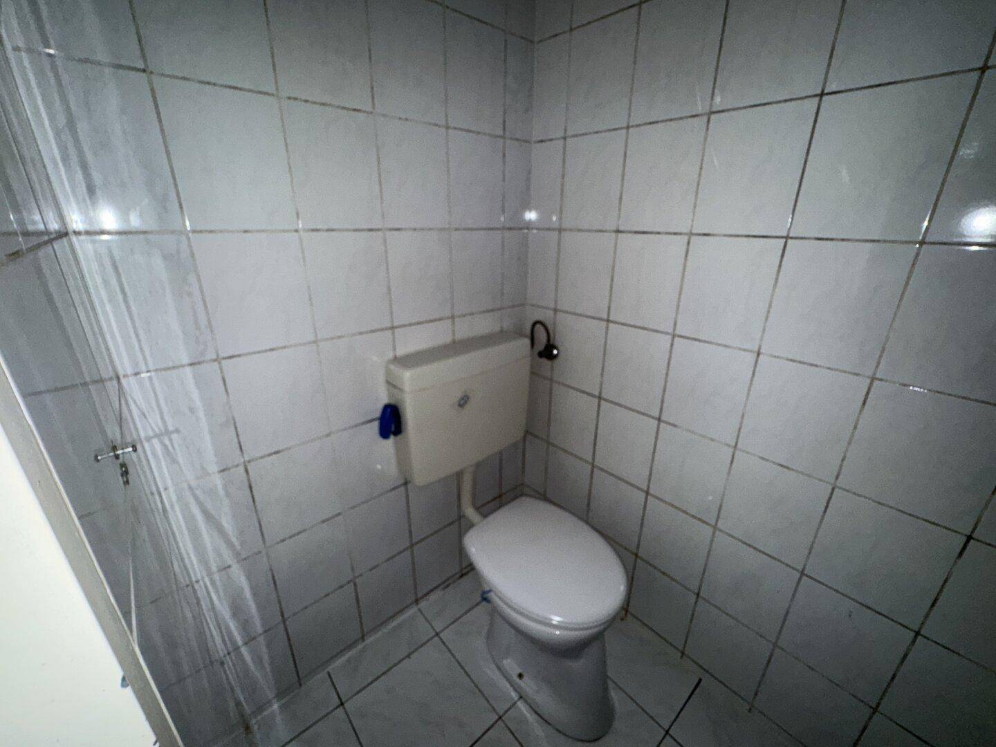 Separate Toilette mit weißen Fliesen und Standard-WC, in einem einfachen, funktionalen Zustand.
