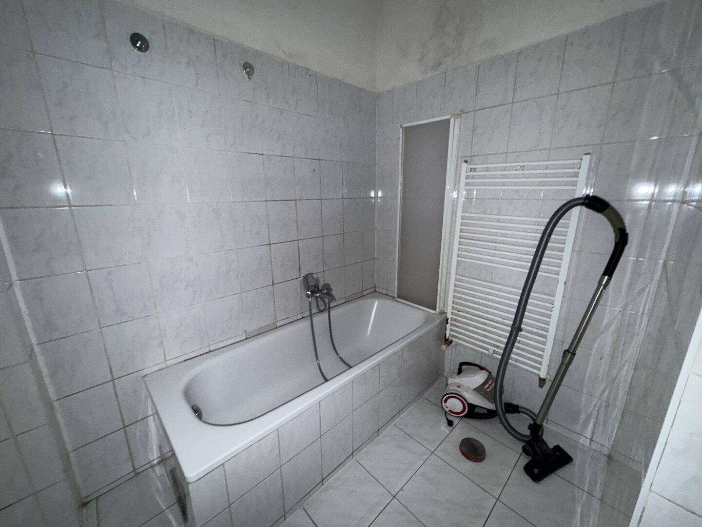 Badezimmer mit Badewanne und Handtuchheizkörper, in einem Zustand, der Modernisierung benötigt.