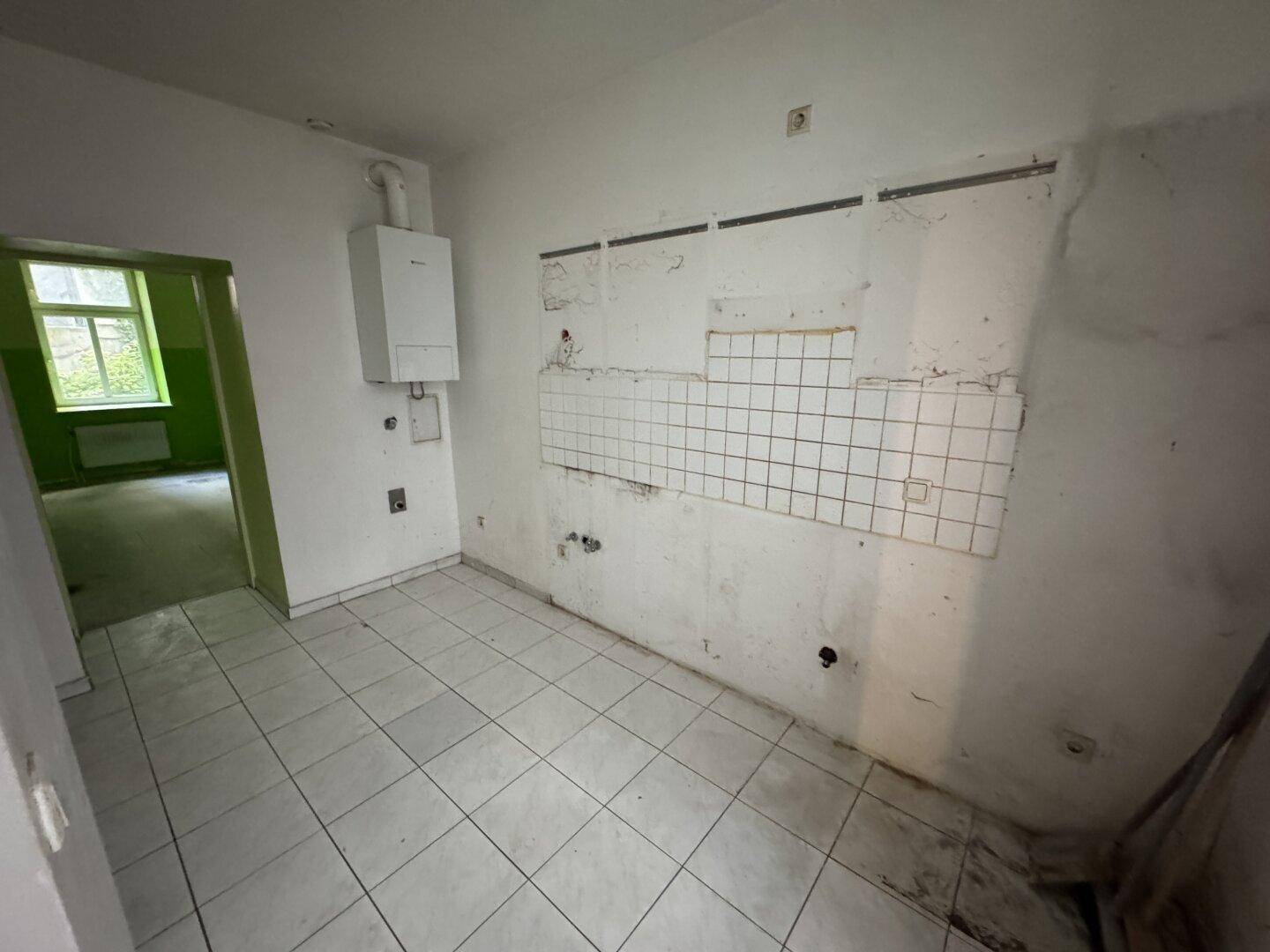 Küche mit Gastherme und Fliesenresten, bereit für eine neue Einbauküche und Modernisierung.