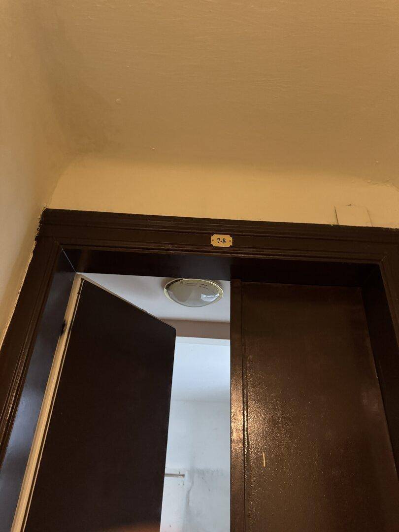 Eingangsbereich mit dunklem Türrahmen und Deckenleuchte, in einem einfachen, älteren Zustand.