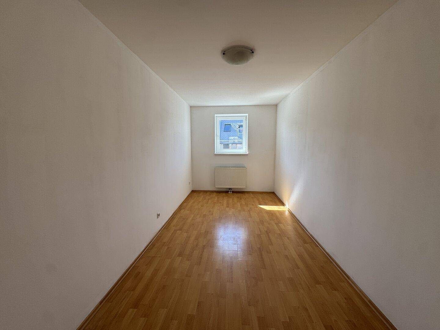 Schmaler Raum mit Parkettboden und einem Fenster, das für natürliches Licht sorgt.