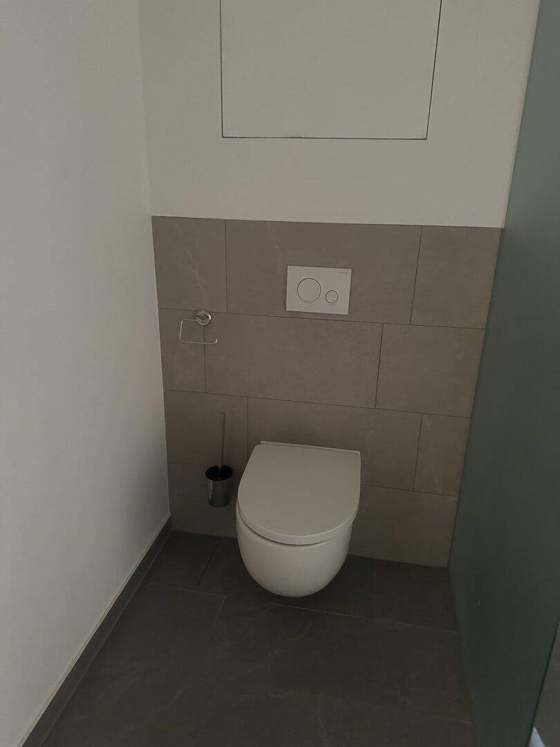 Separates WC mit wandhängender Toilette und modernen grauen Fliesen an Wand und Boden.
