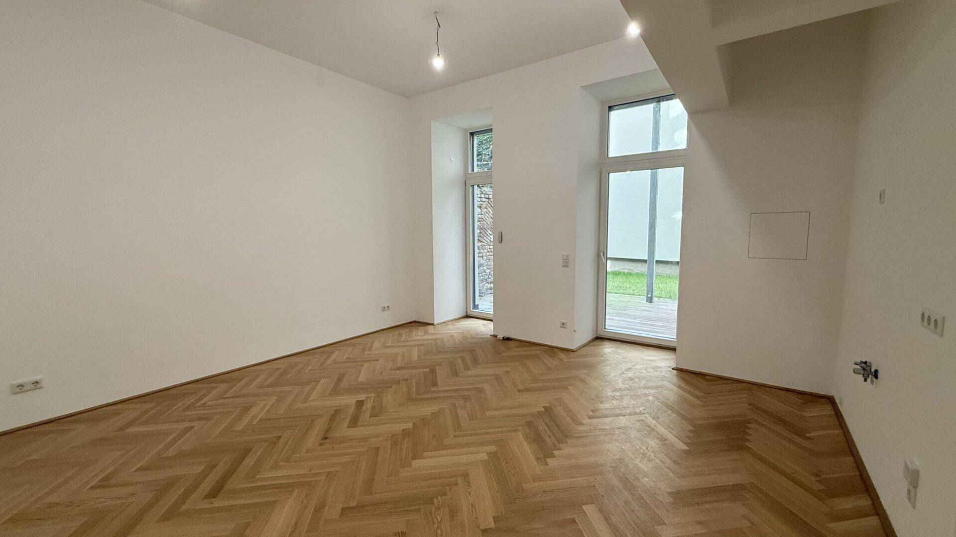 Geräumiger Wohnbereich mit klassischem Fischgrätparkett und viel Tageslicht durch die Fenstertüren.