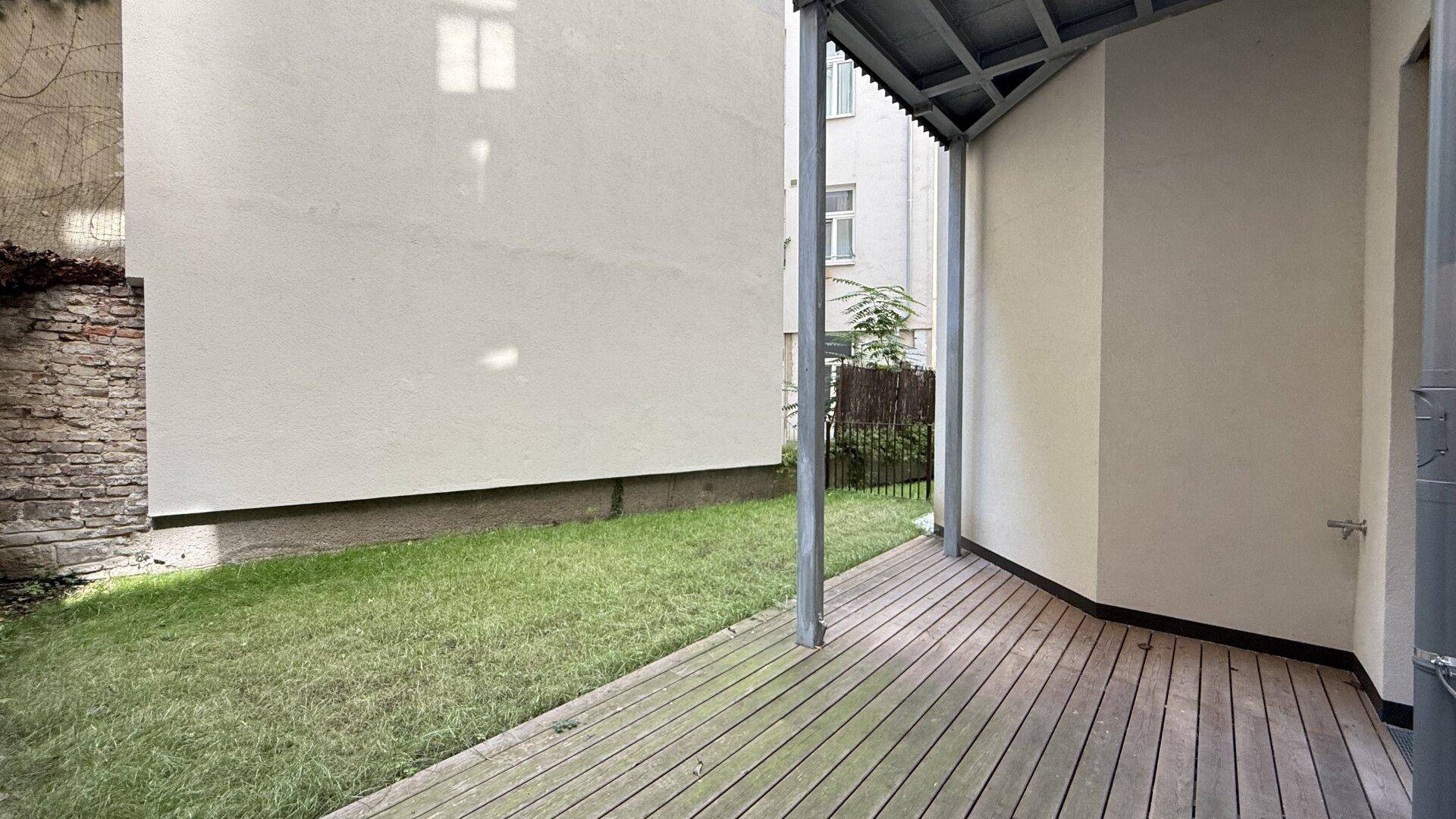 Überdachte Loggia mit Holzbelag und angrenzender Rasenfläche, ideal für entspannte Stunden im Freien.