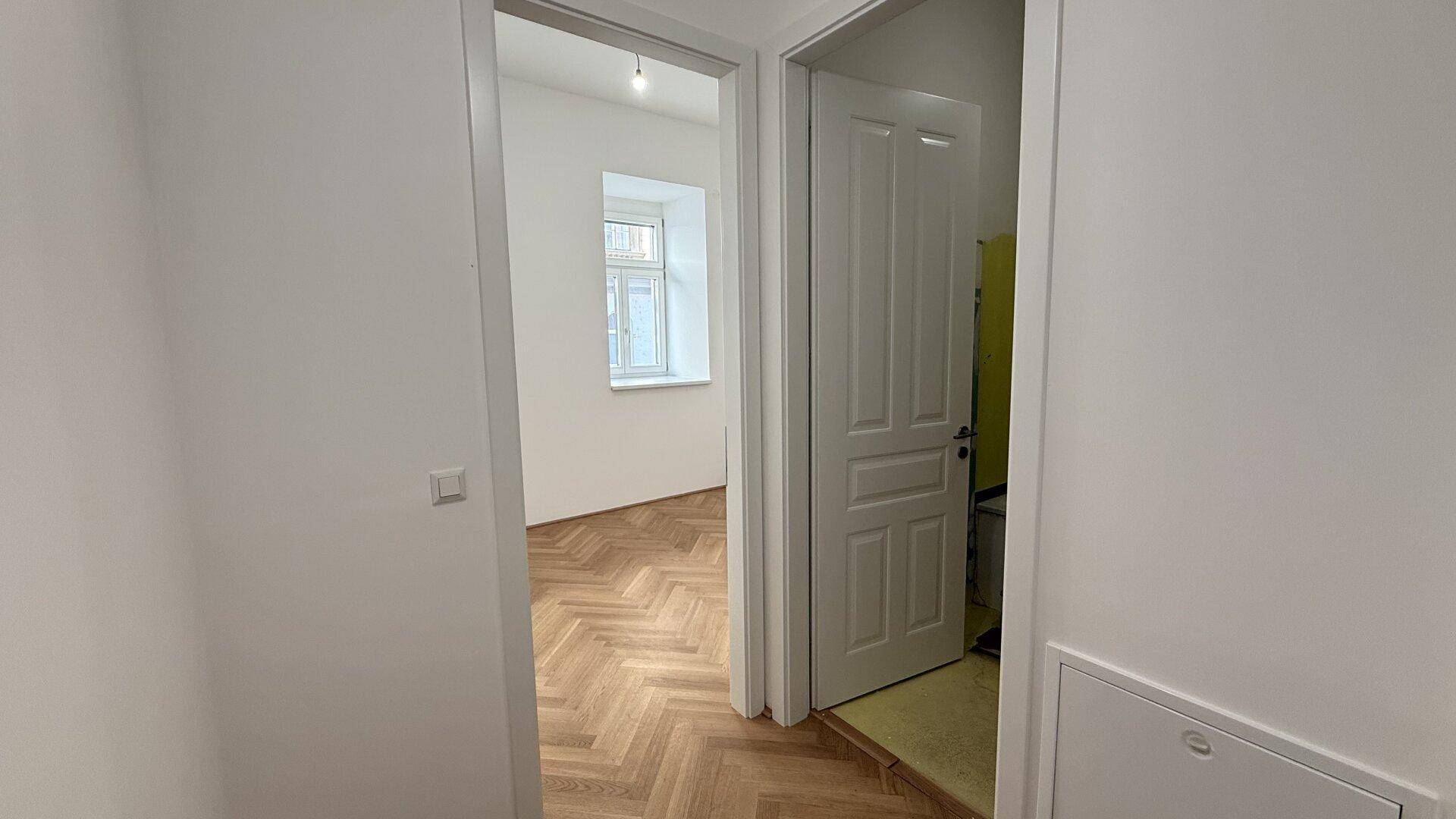 Heller Flur mit weiß gestrichenen Wänden und Zugang zu weiteren Räumen mit Parkettboden.