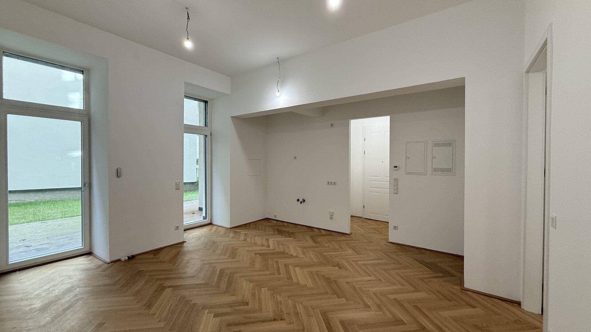 Heller Wohnraum mit elegantem Fischgrätparkett und großen Fenstertüren zum Außenbereich.