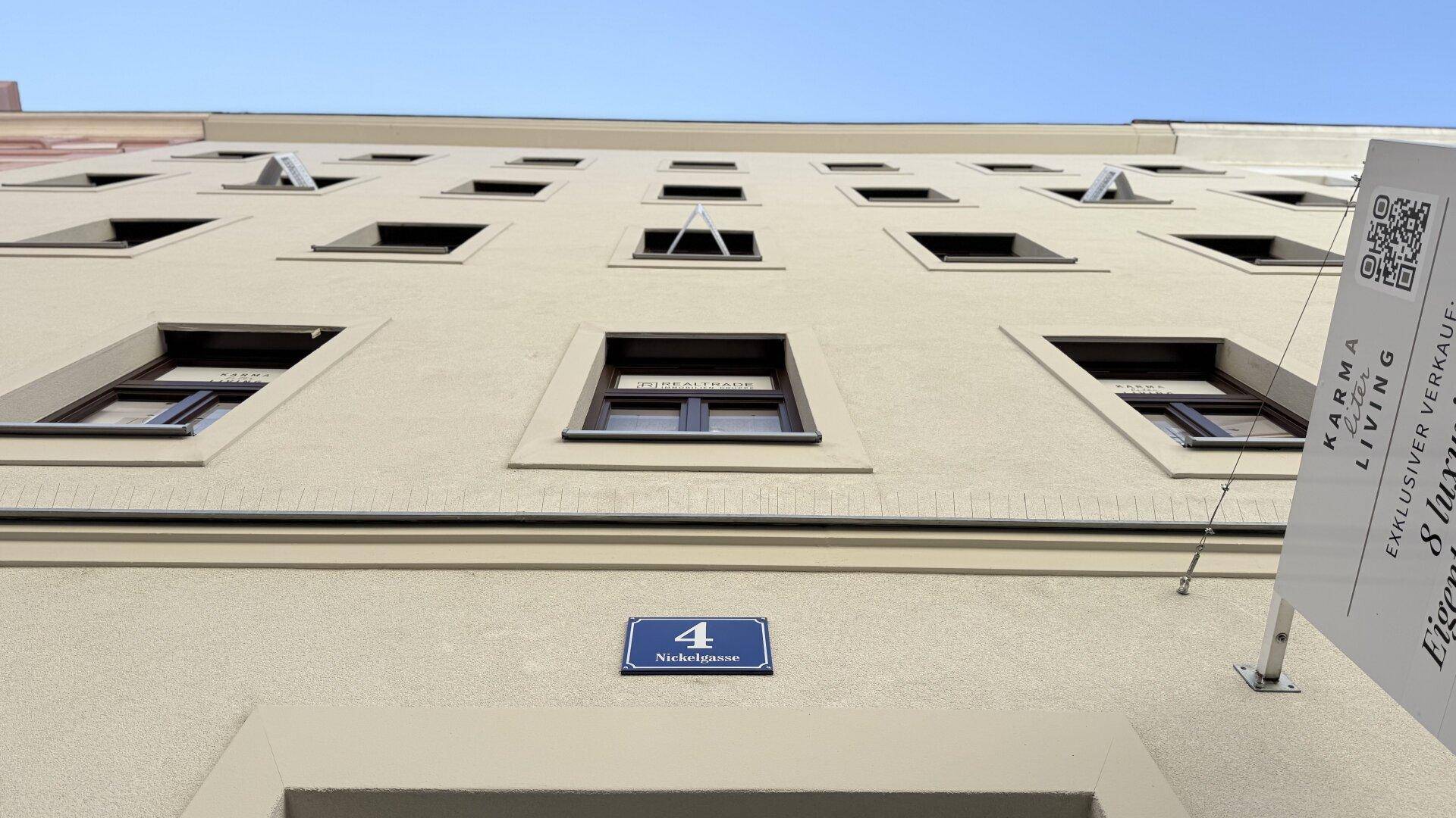 Fassade eines Mehrfamilienhauses mit zahlreichen Fenstern und Verkaufsanzeigen, von unten betrachtet.