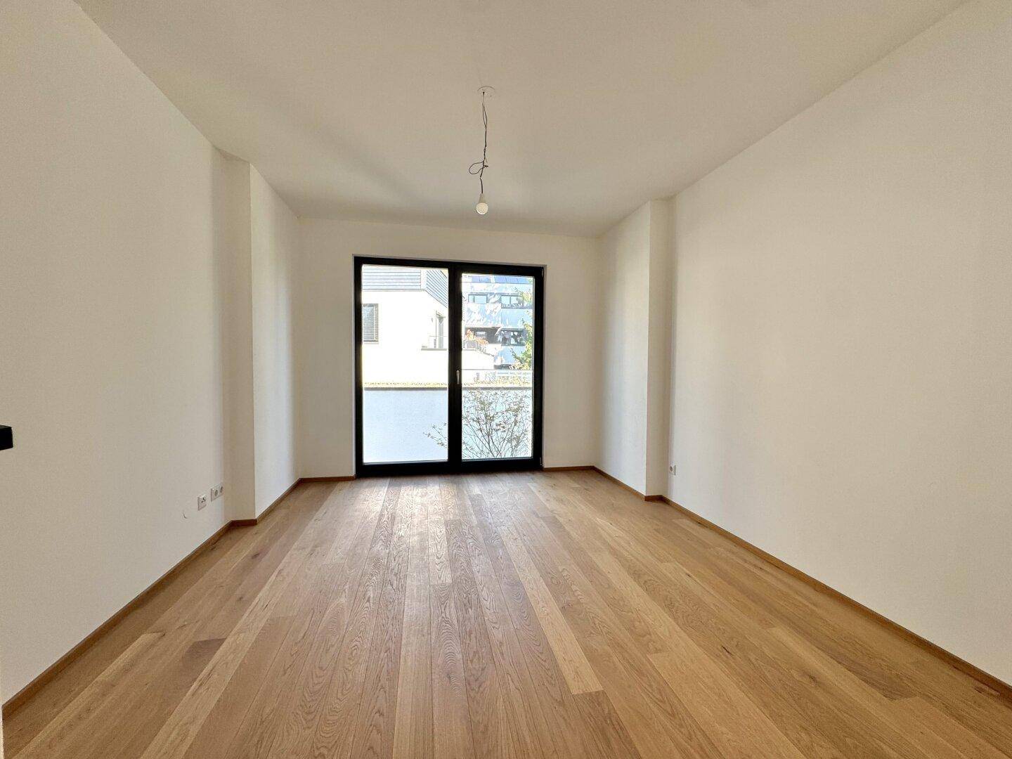 Geräumiges Zimmer mit Holzboden und großen Fenstern, die viel Tageslicht hereinlassen.