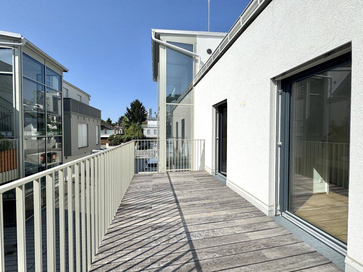 Geräumiger Balkon mit Holzboden und Blick auf moderne Architektur unter blauem Himmel.