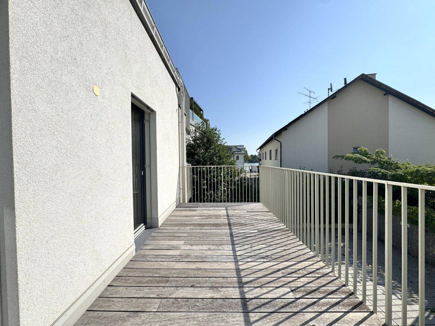 Sonniger Balkon mit Holzboden und Blick auf die ruhige Wohngegend und grüne Umgebung.
