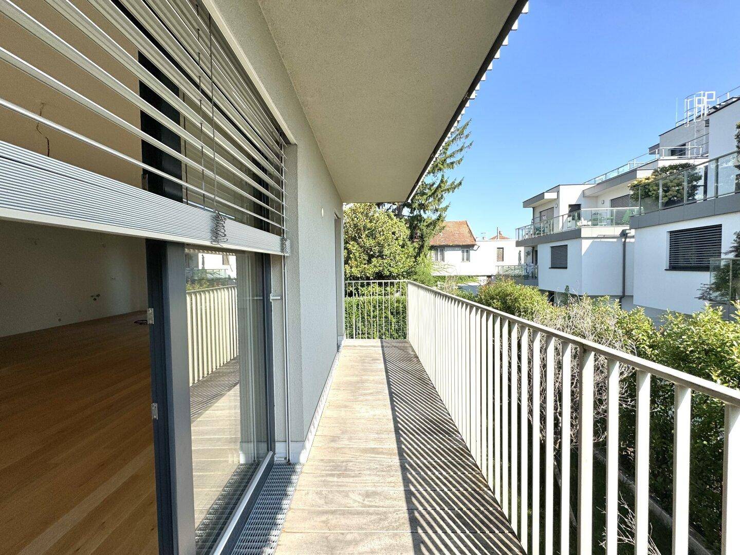 Heller Balkon mit Holzdielen und Blick auf die umliegenden modernen Gebäude und Grünflächen.