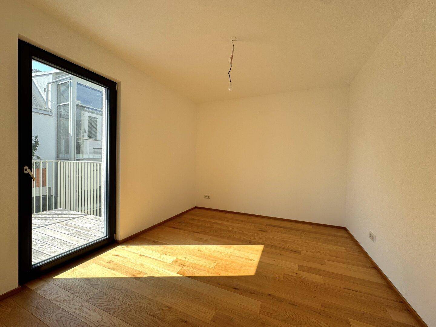 Sonniger Raum mit Holzboden und direktem Zugang zu einem Balkon, perfekt für ein Schlafzimmer.